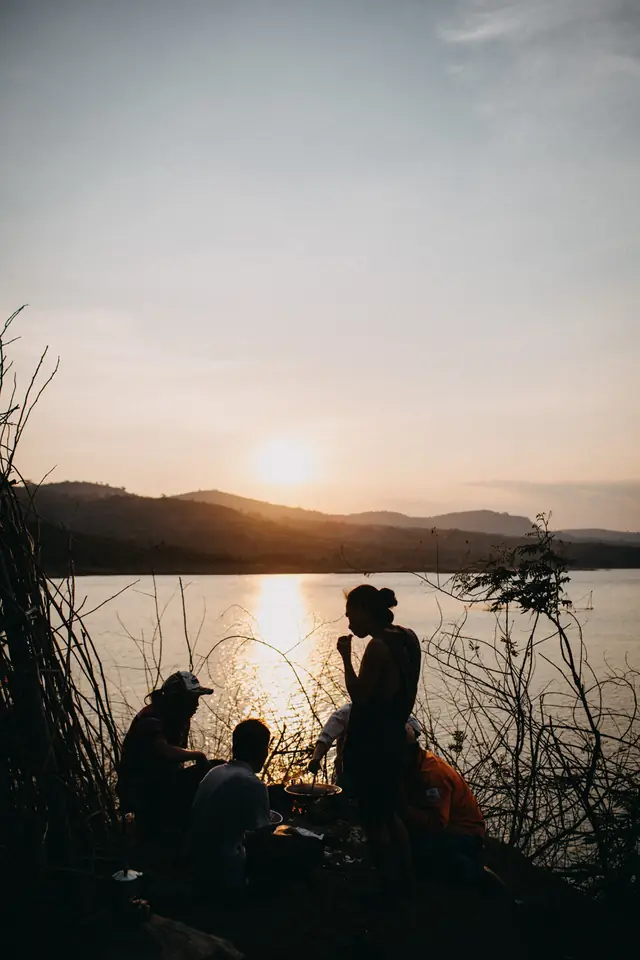 Friends cooking dinner beside a lake at sunset