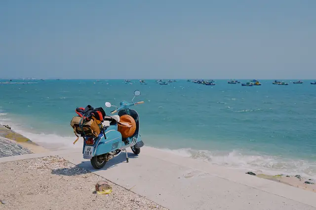 A vintage Vespa loaded with travel bags parked by the sea