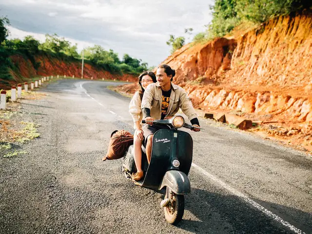 A couple riding a vintage Vespa on a red-dirt mountain road