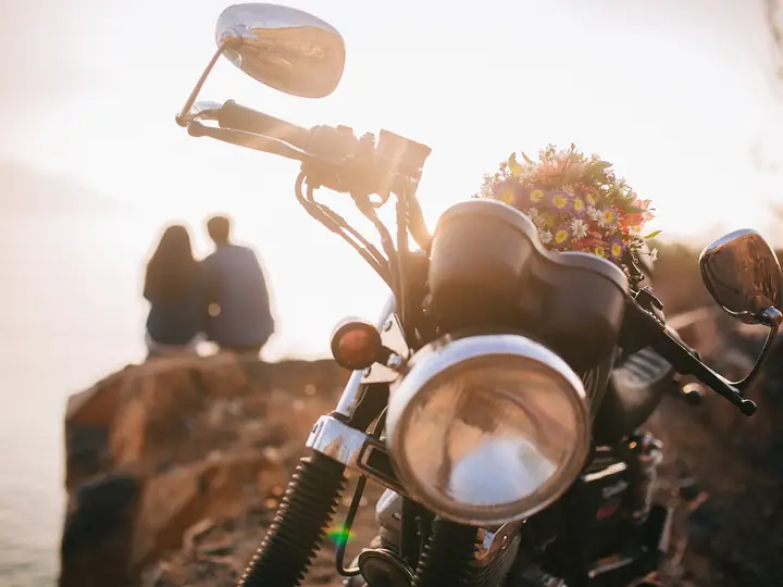 A motorbike with flowers on the handlebars, a couple watching the sunset behind it