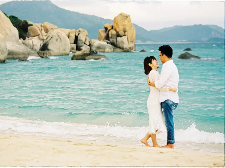 A couple embracing on a beach with turquoise water and granite rocks