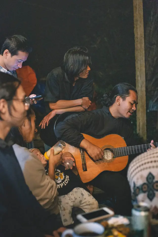 A man singing with a guitar at a night gathering of friends